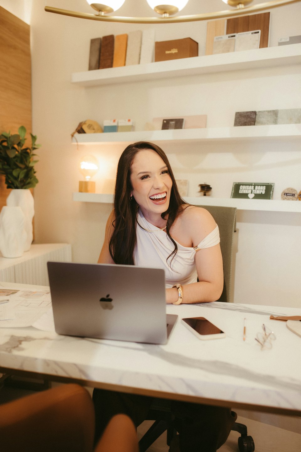 Donna sorride mentre lavora al laptop su una scrivania di marmo.